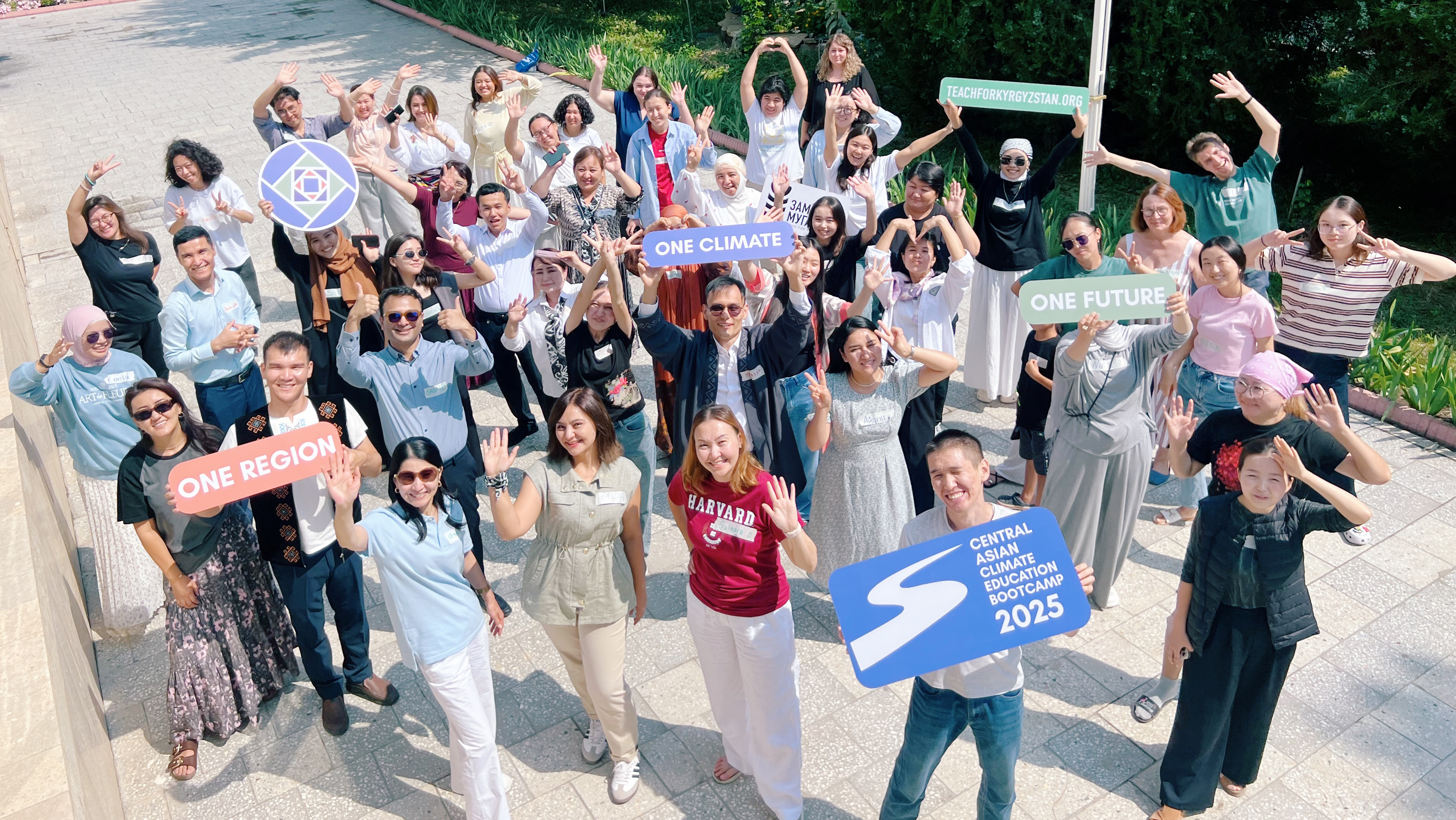 A group of adults stand outside. They are holding up signs that read "One Region," "One Climate," "One Future" and "Central Asian Climate Bootcamp 2025"